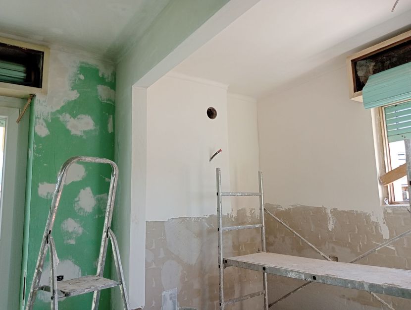 Stanza in fase di ristrutturazione con pareti verdi e bianche, scala e impalcature.