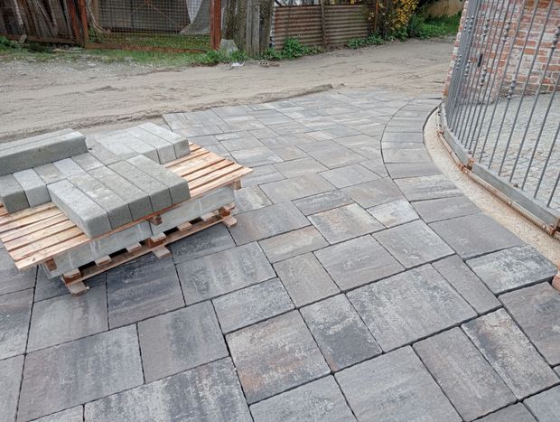 Posa di lastricati grigi, con un bancale di nuove pietre nelle vicinanze. Bordo curvo del sentiero con struttura in metallo.