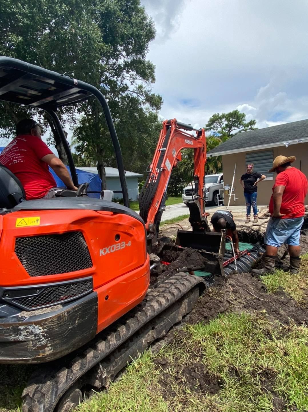 Workers installing septic system with an orange excavator in a yard on a sunny day.