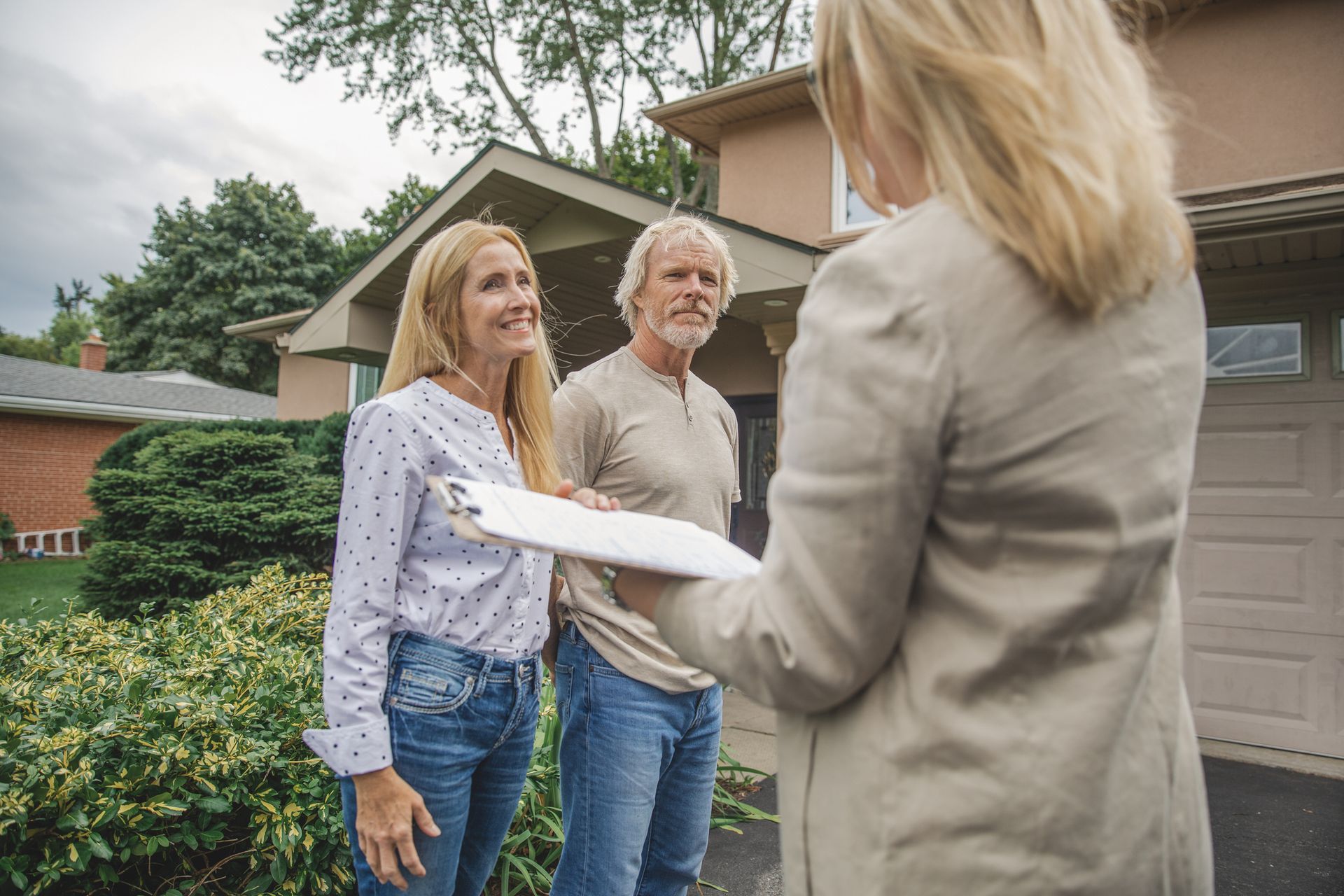 Real estate agent showing paperwork to a couple in front of a house.