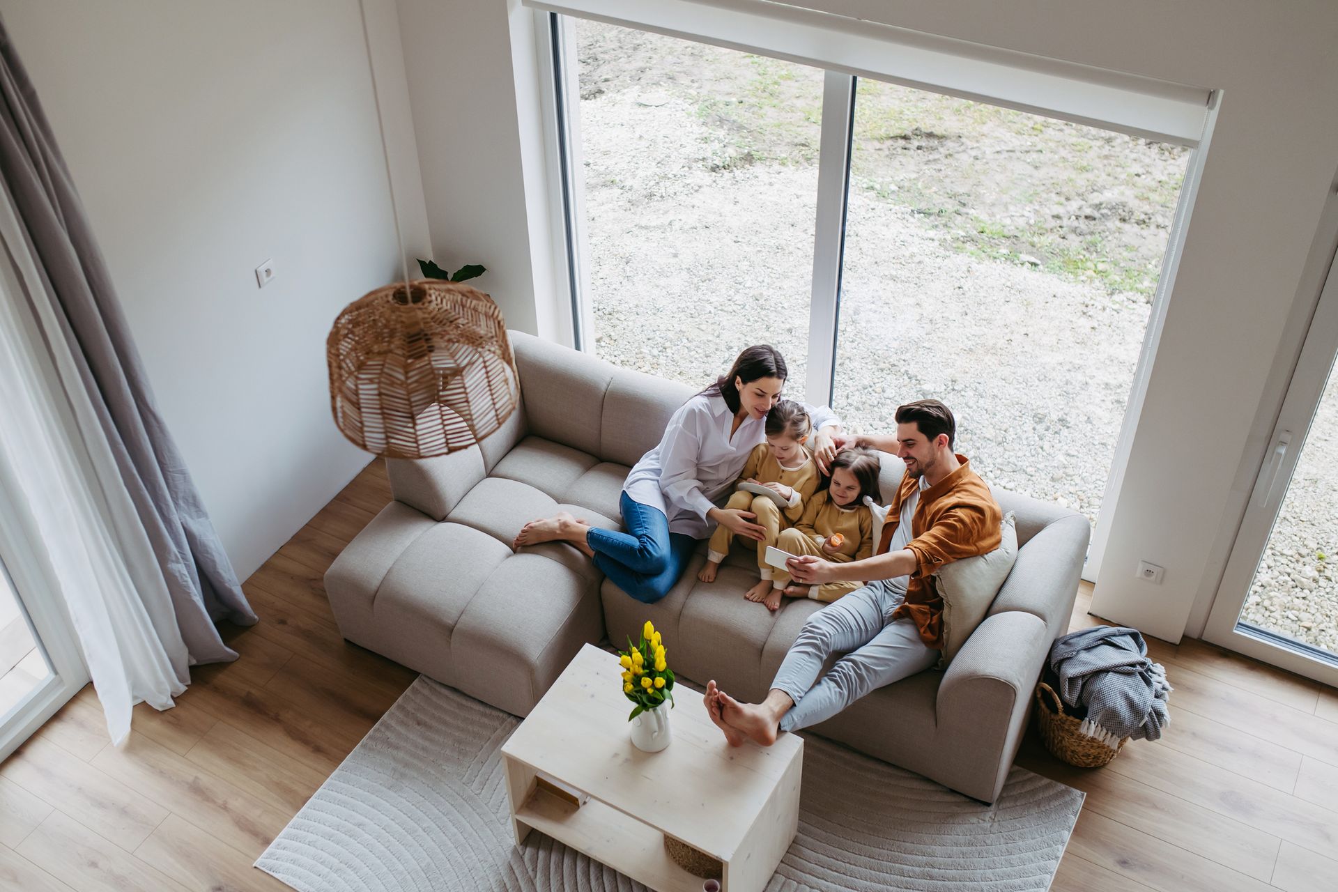Family of four relaxing on a beige sofa in a bright living room, enjoying time together.
