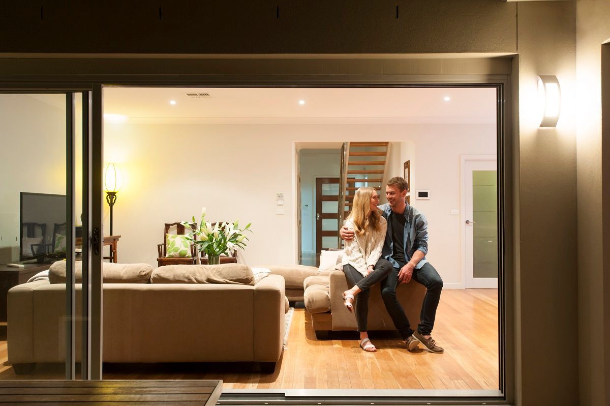 Couple sits on a sofa in a warmly lit living room, visible through sliding glass doors at night.