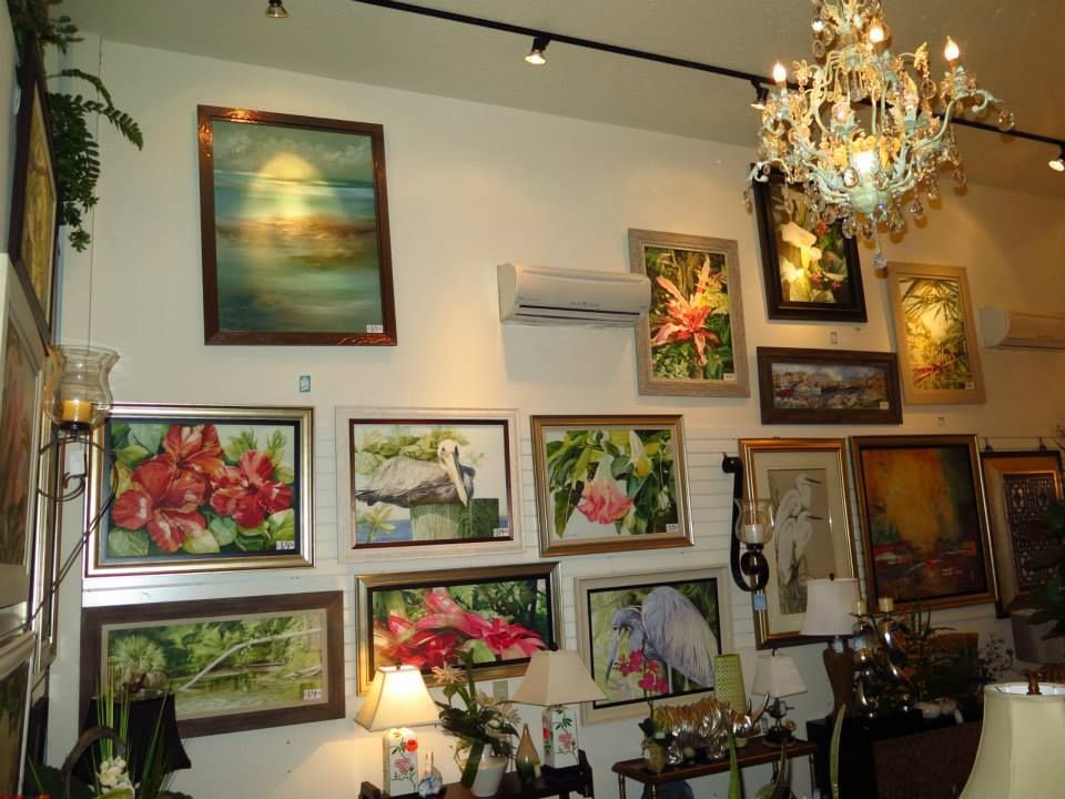 White gallery wall with framed floral and landscape paintings, chandelier, track lighting.