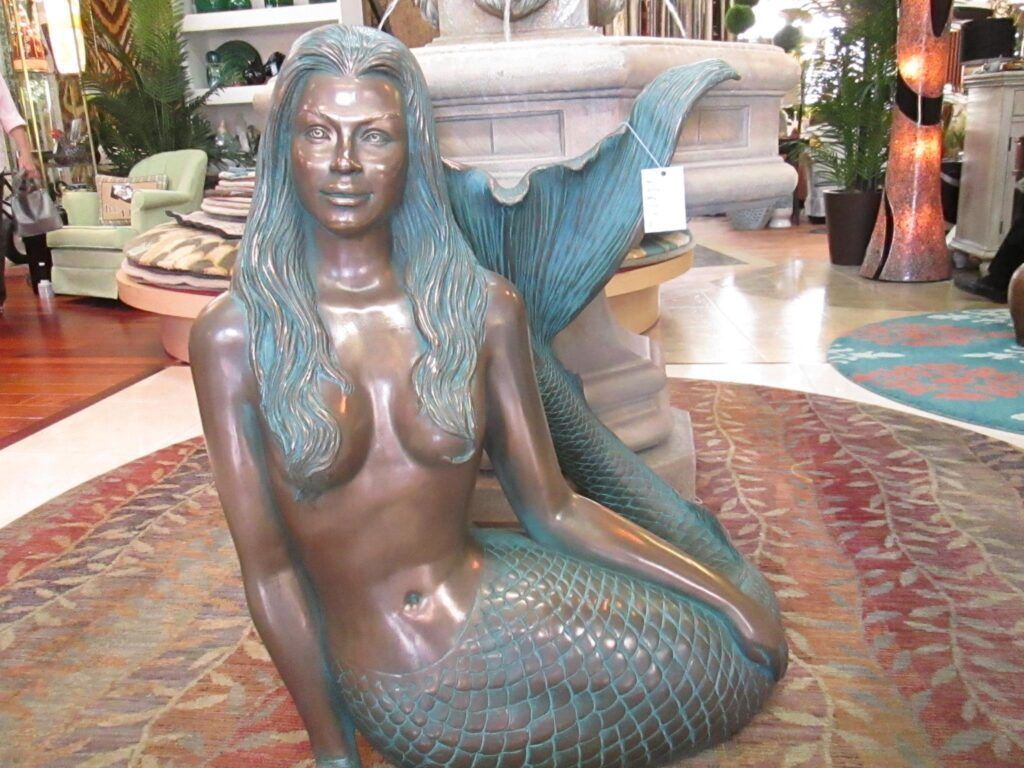 Bronze mermaid sculpture, green-blue tail, on a patterned rug, in a store.