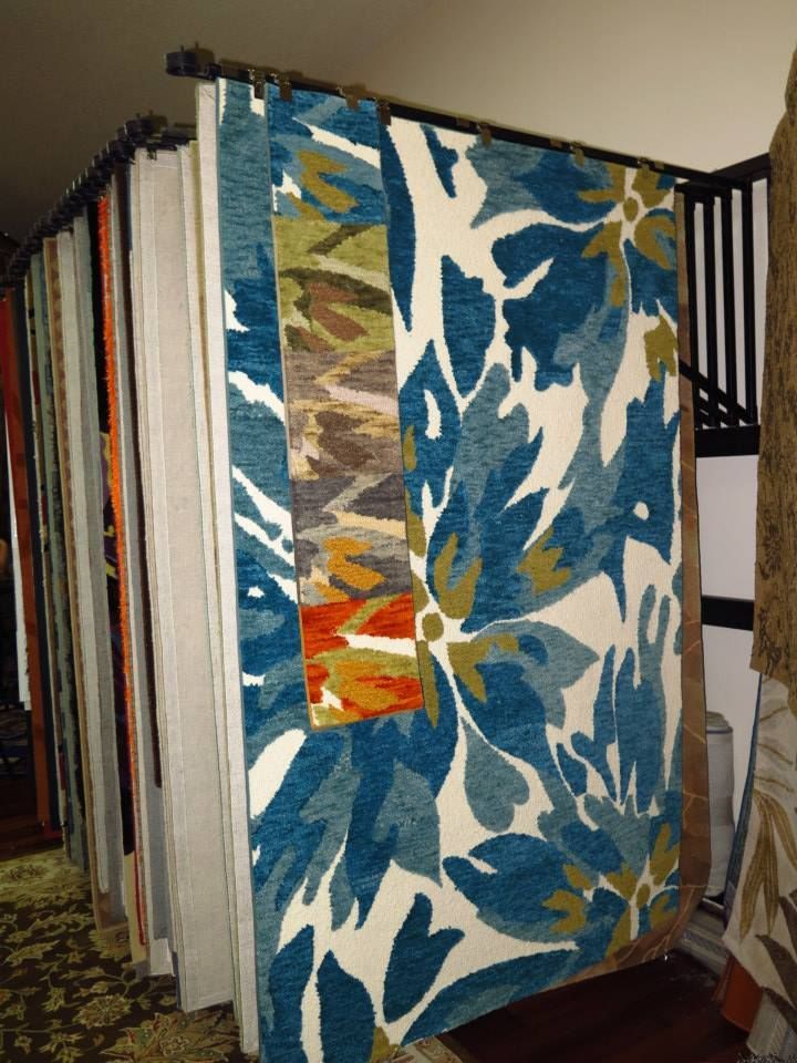 Rugs hanging on display, showcasing various patterns and colors, including blue floral.