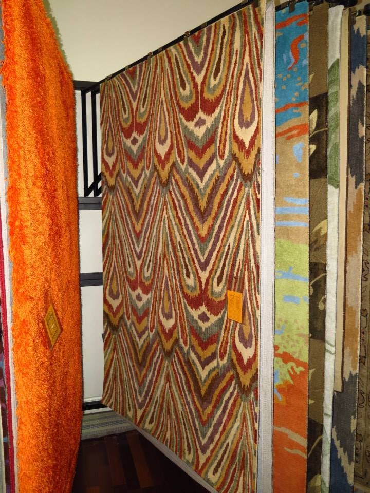 Rugs on display: orange, patterned zigzags, blue, green, and other colorful designs.
