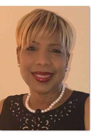 A woman wearing a black dress and a pearl necklace is smiling.