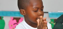 A young boy is praying with his hands together in a classroom.