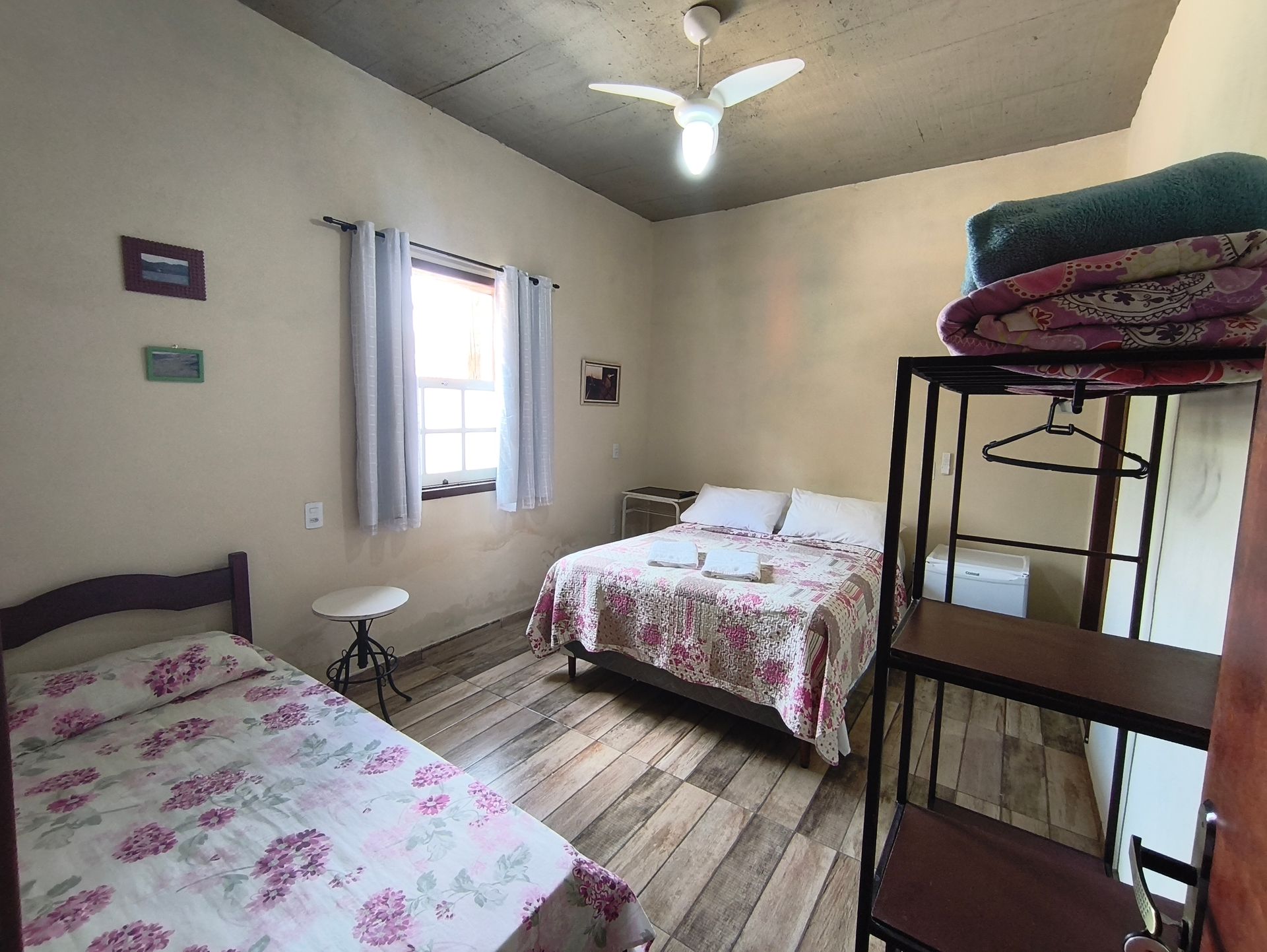 Quarto com duas camas, janela, prateleiras de metal e teto de concreto.