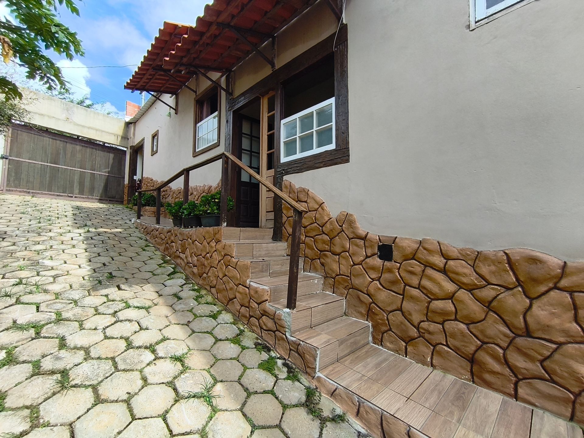Prédio bege com fachada de pedra, degraus de madeira que levam à entrada, calçada pavimentada à esquerda.