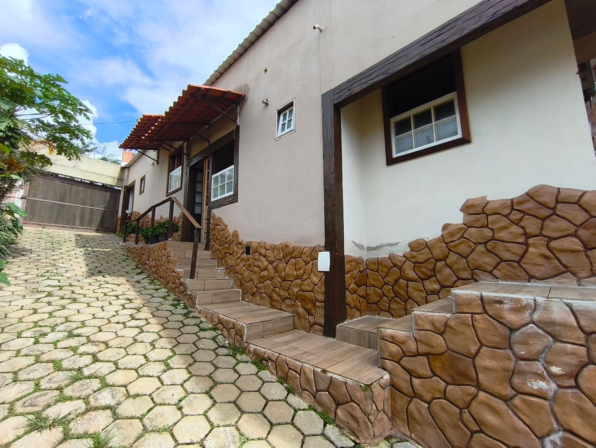 Prédio com fachada de pedra marrom, degraus e rampa com caminho de paralelepípedos.