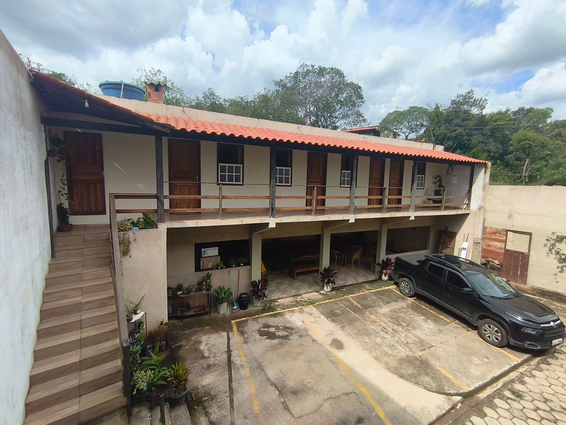 Prédio de dois andares com varanda coberta e estacionamento. Carro preto estacionado em frente.