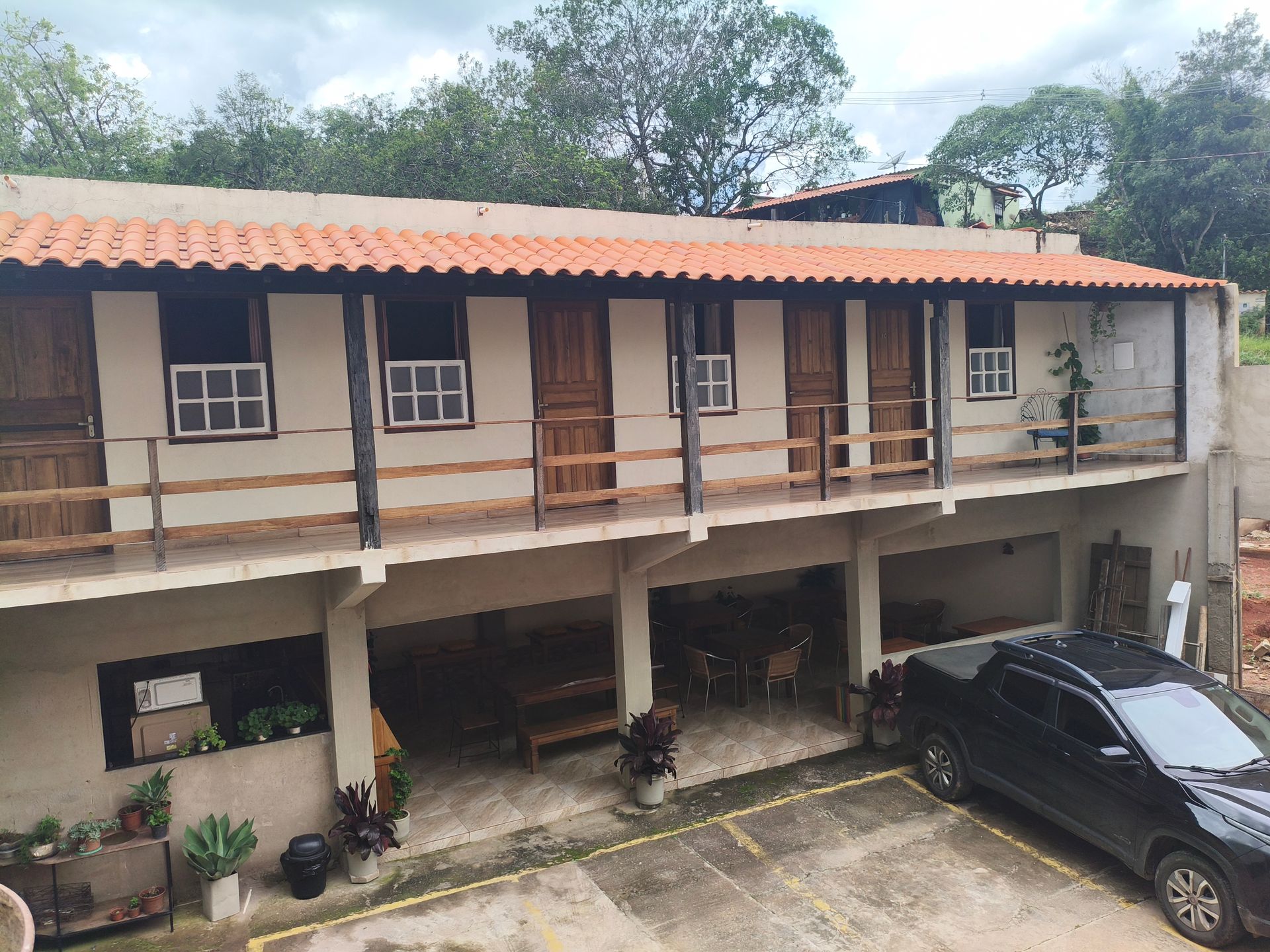 Prédio de dois andares com quartos, varanda e estacionamento. Portas e janelas marrons, carro preto na frente.