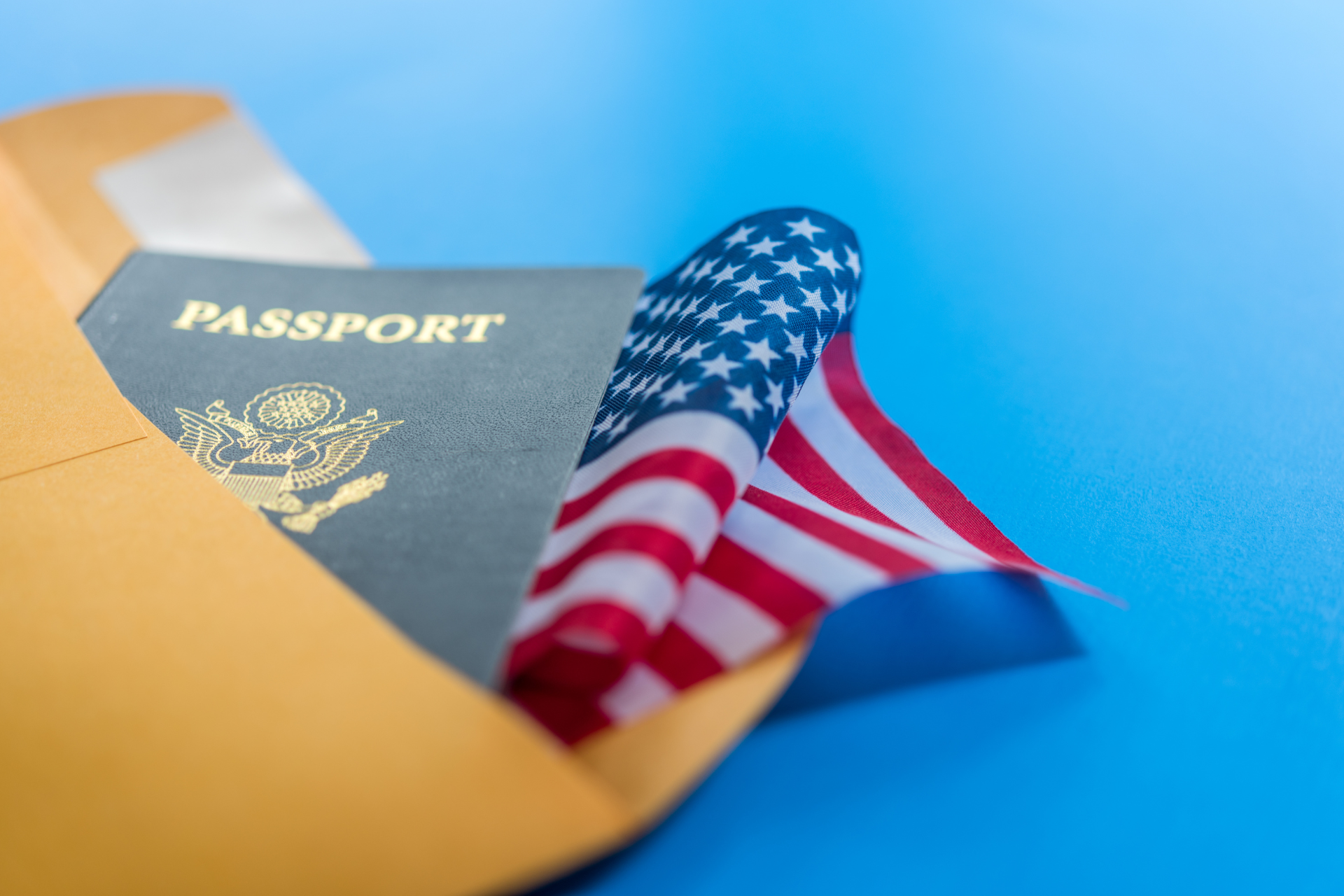 Passport and folded American flag emerging from a manila envelope on a blue background.