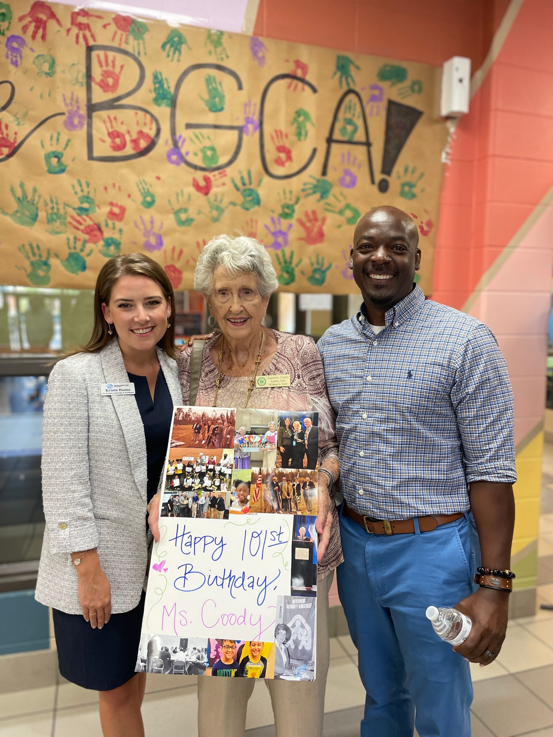 CEO Kristin Hanna and Site Director Charles Williams celebrate. Ms. Coody's 100th birthday with a poster.
