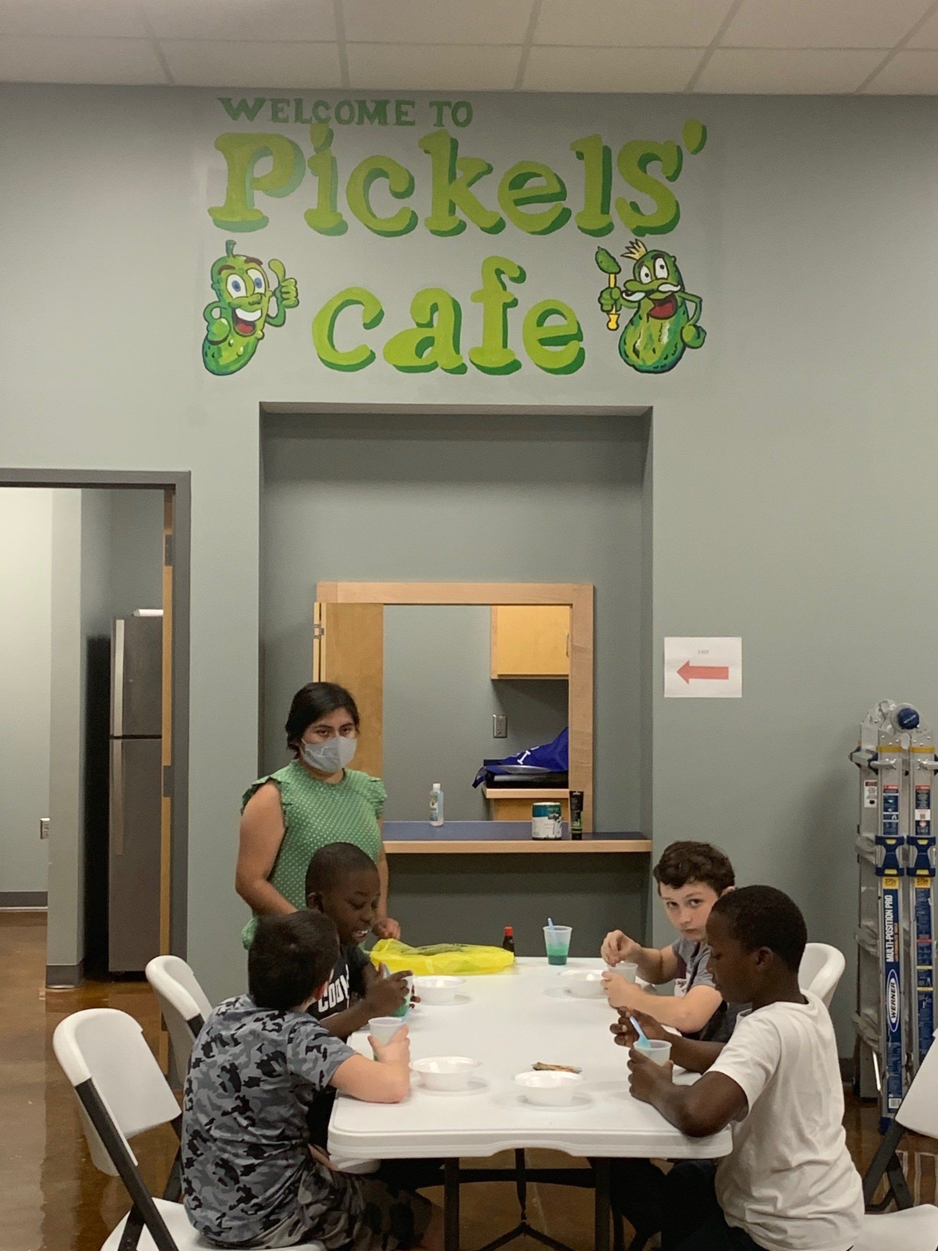 Children and an adult in a cafe painting at a table. 