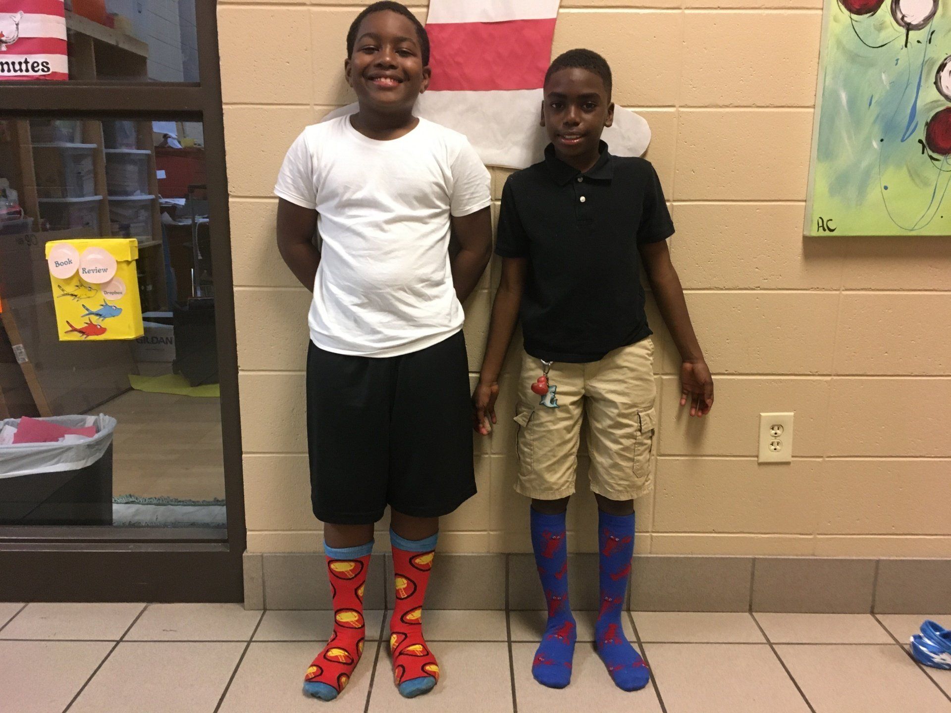 Two boys smiling, wearing colorful socks, standing in a hallway.