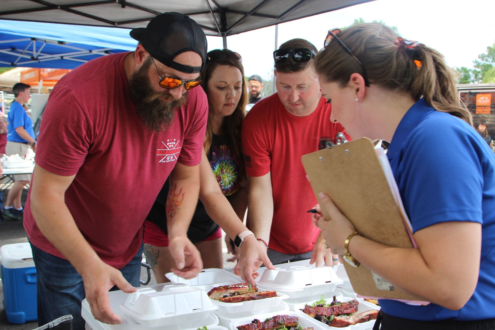 Four people at a food competition: judging BBQ ribs at an outdoor event.