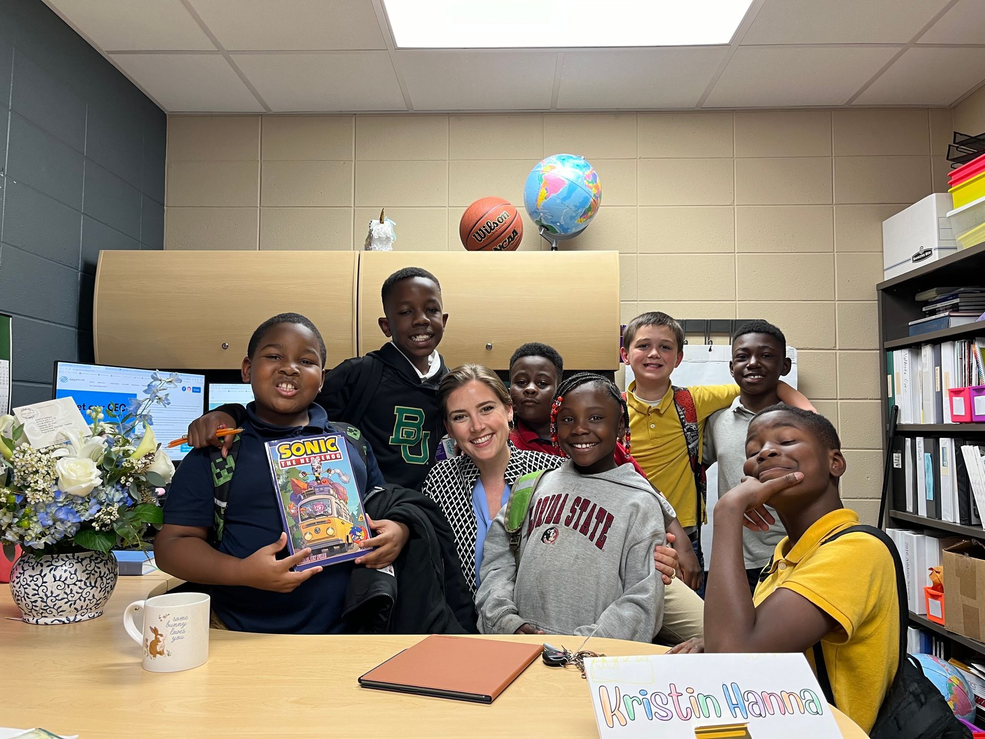 CEO Kristin Hanna and students smiling and posing in an office. Students are hugging and holding a book.