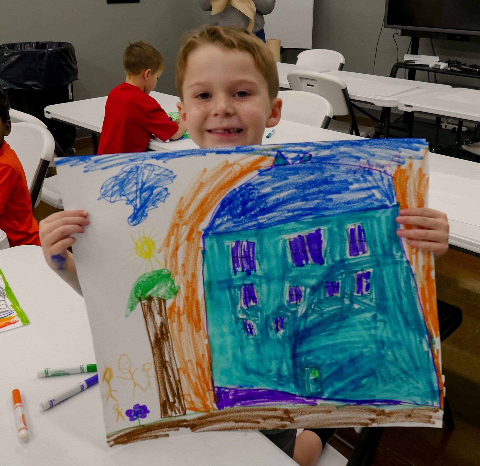 Boy holding a colorful crayon drawing of a house at Boys & Girls Club