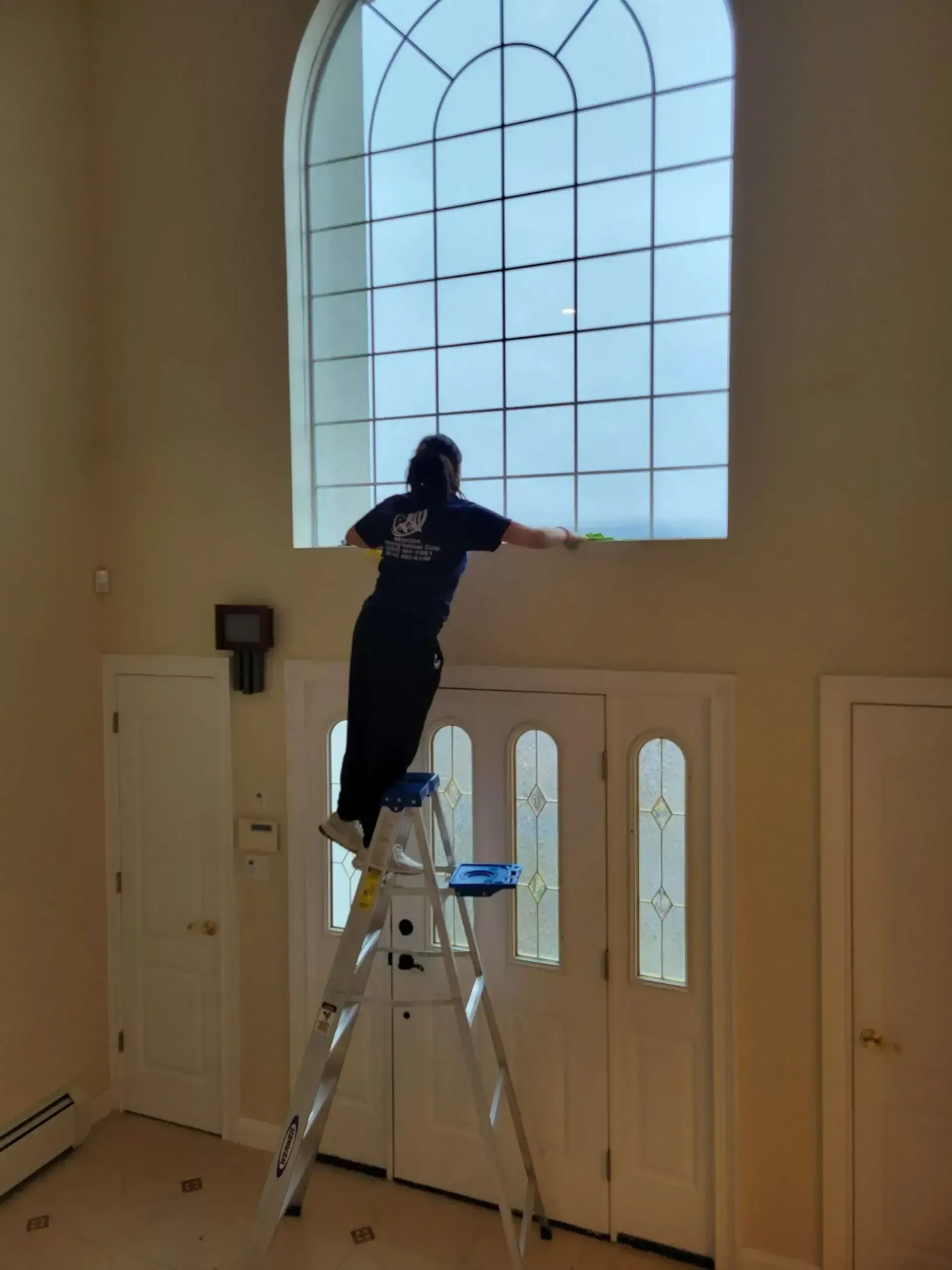 A woman is standing on a ladder cleaning a window.