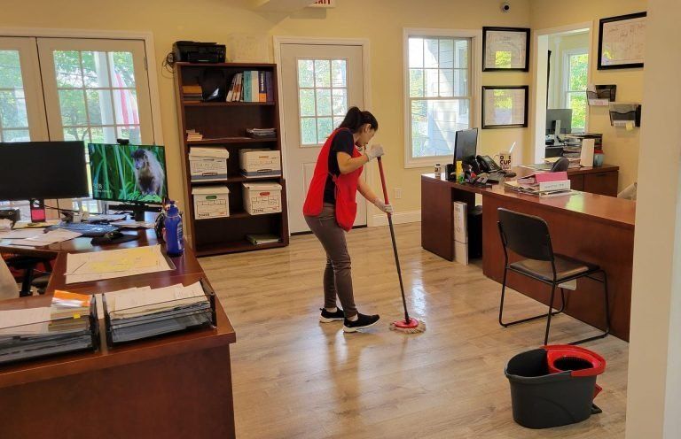 A woman is cleaning the floor of an office with a mop.
