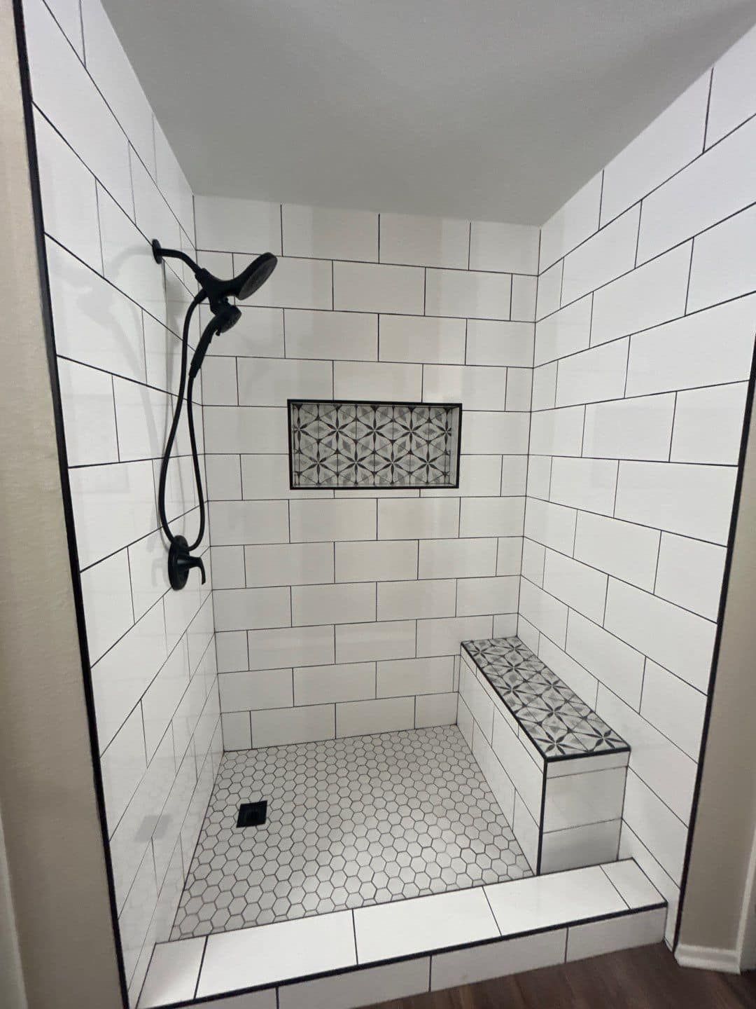 A shower with white tiles and a black shower head