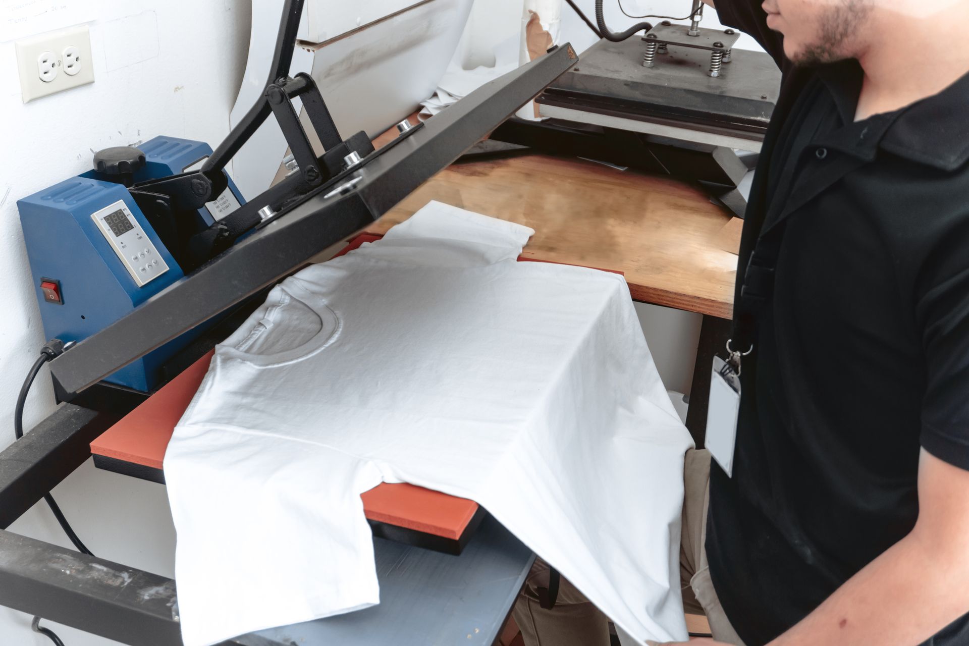 Man presses a white t-shirt on a heat press machine in a workshop.