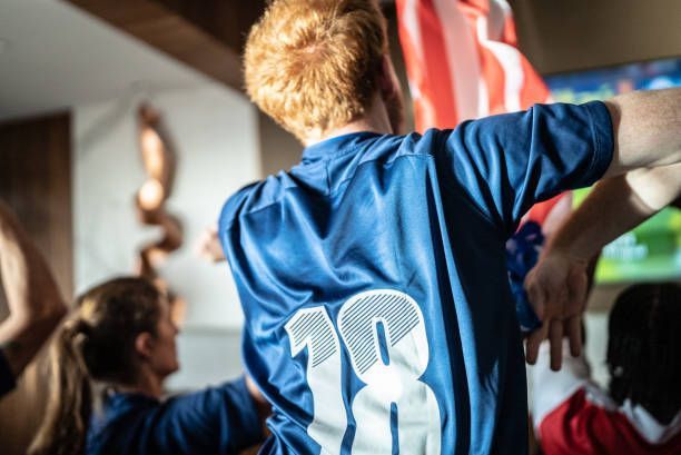 People celebrating in a room, one holding an American flag, jersey with the number 18.