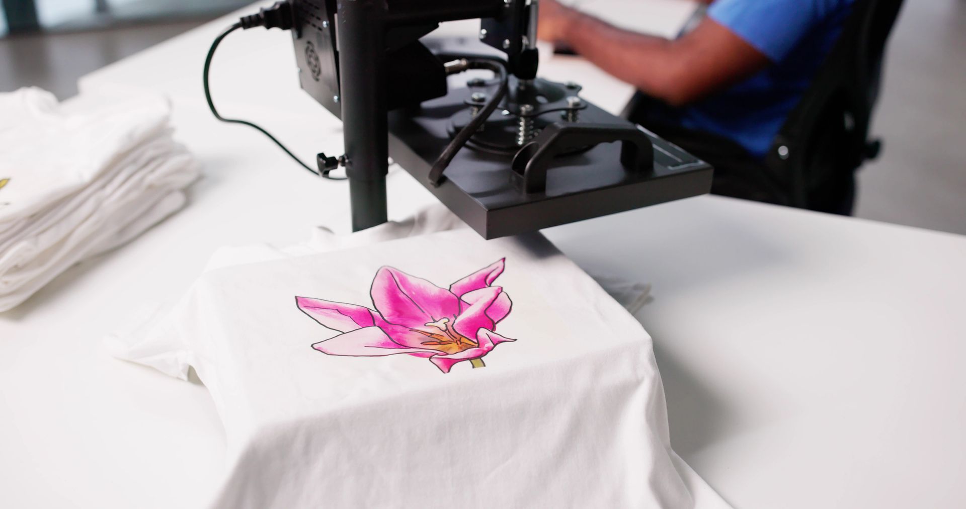 A person using a heat press to transfer a pink flower design onto a white t-shirt.