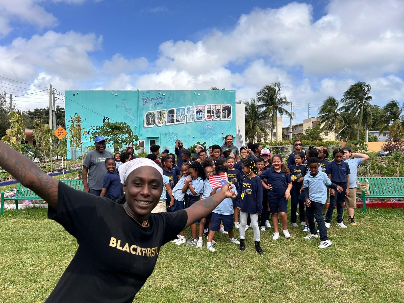 A man in a black shirt is standing in front of a group of children.