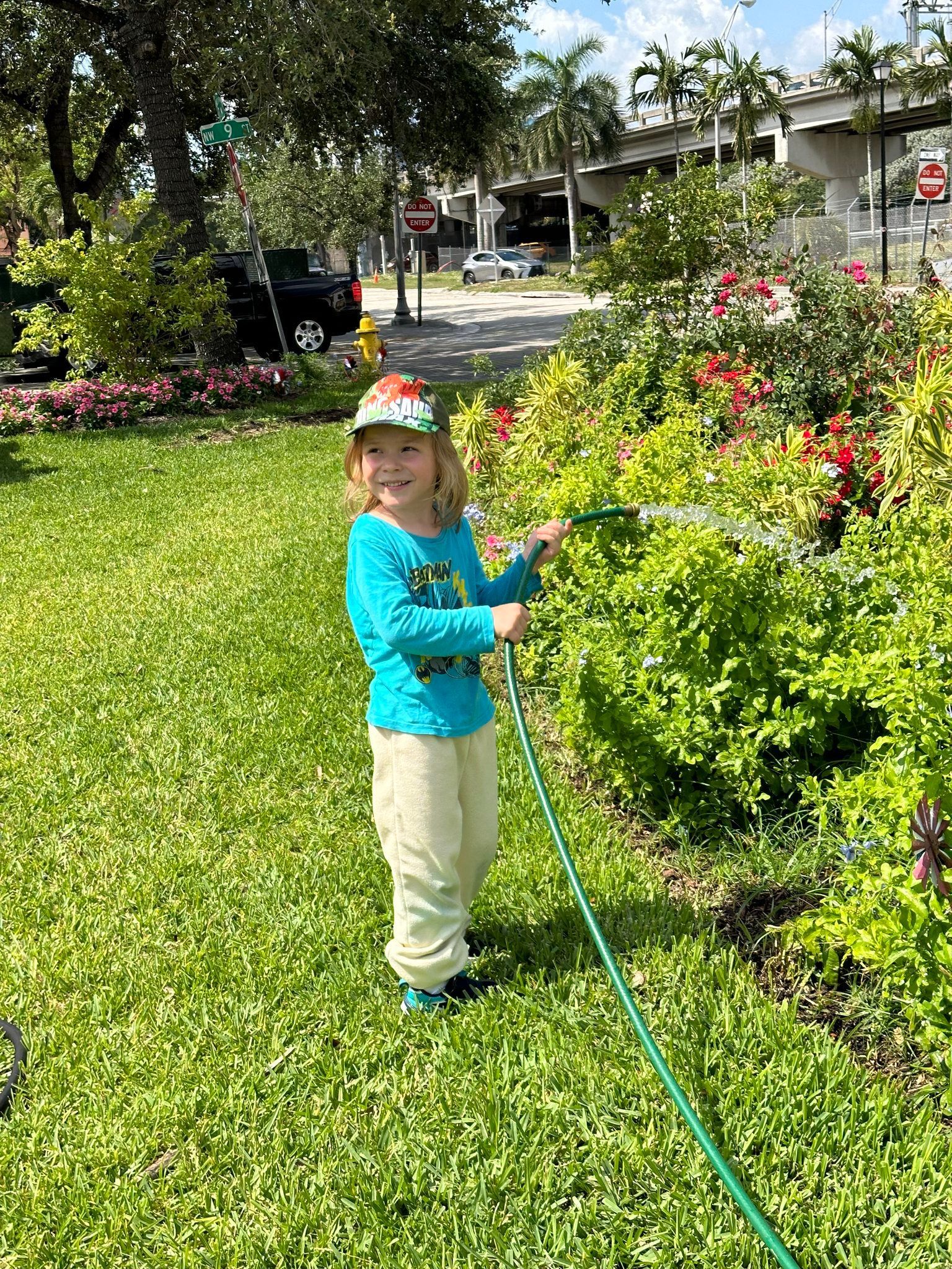 A little girl is watering plants with a hose in a park.