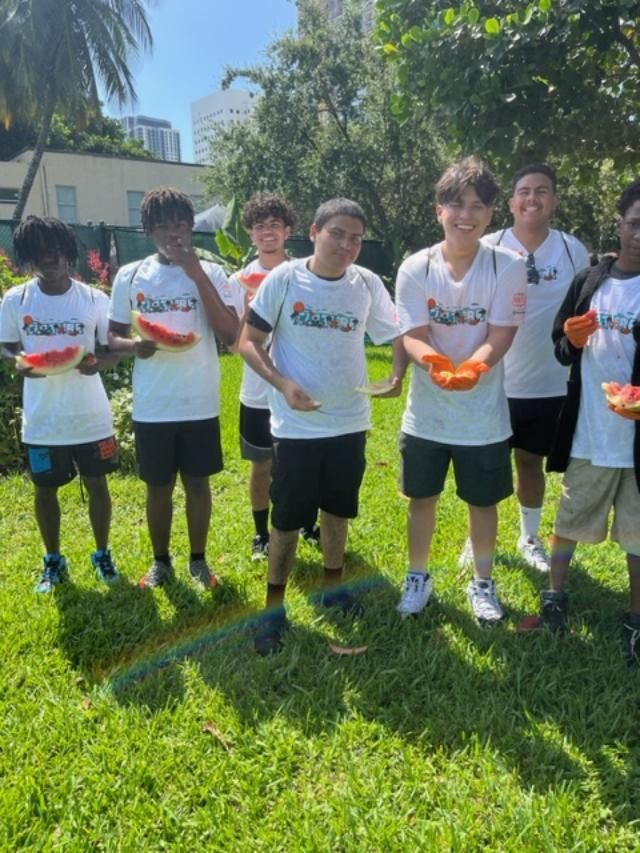 A group of young men are standing in the grass eating watermelon slices.