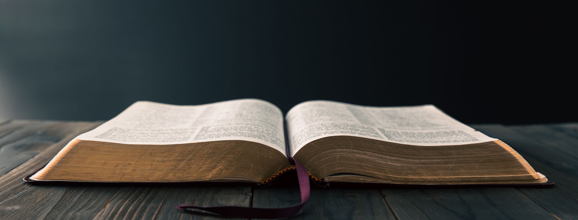 People holding hands over open Bibles on a wooden table, in prayer.