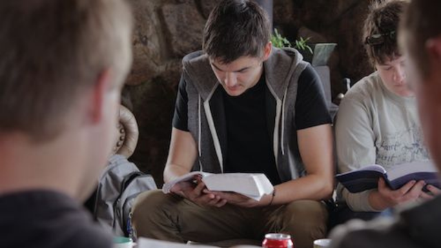 Group of people reading books, seated in a room, focused on texts.