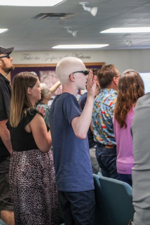 People facing a cross on a stage during a religious service. Some raise their hands.