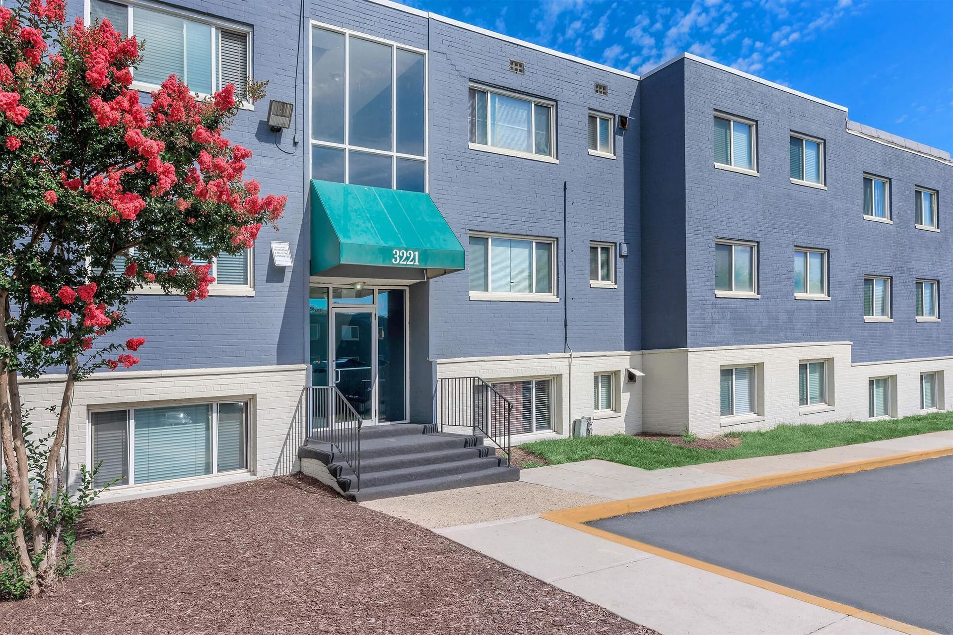 A large apartment building with a green awning and a tree in front of it.