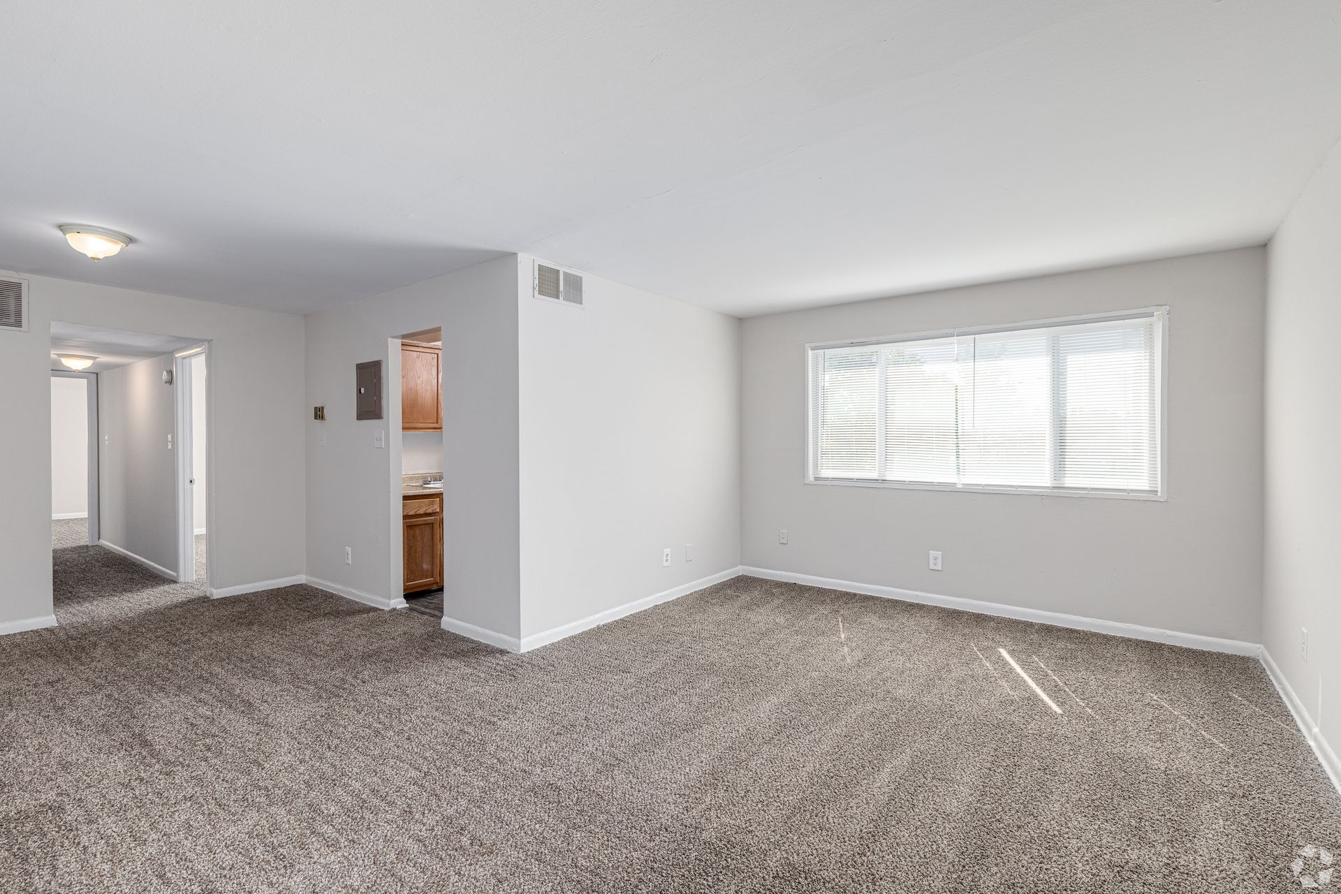 An empty living room with a large window and a carpeted floor.