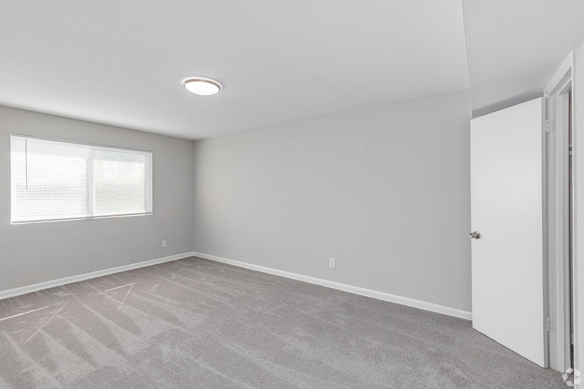 An empty bedroom with a window and a door.