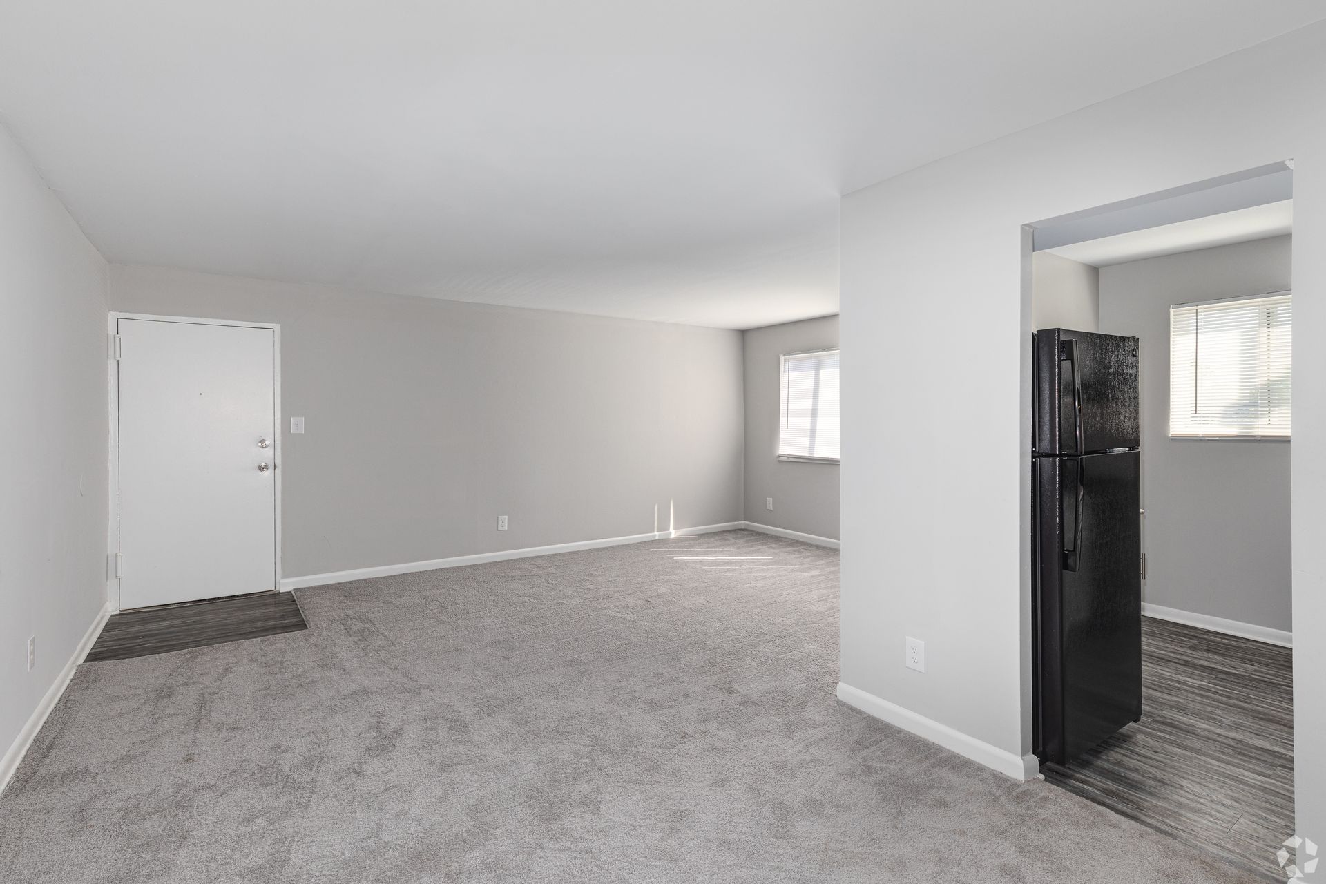An empty living room with a refrigerator and a black refrigerator.