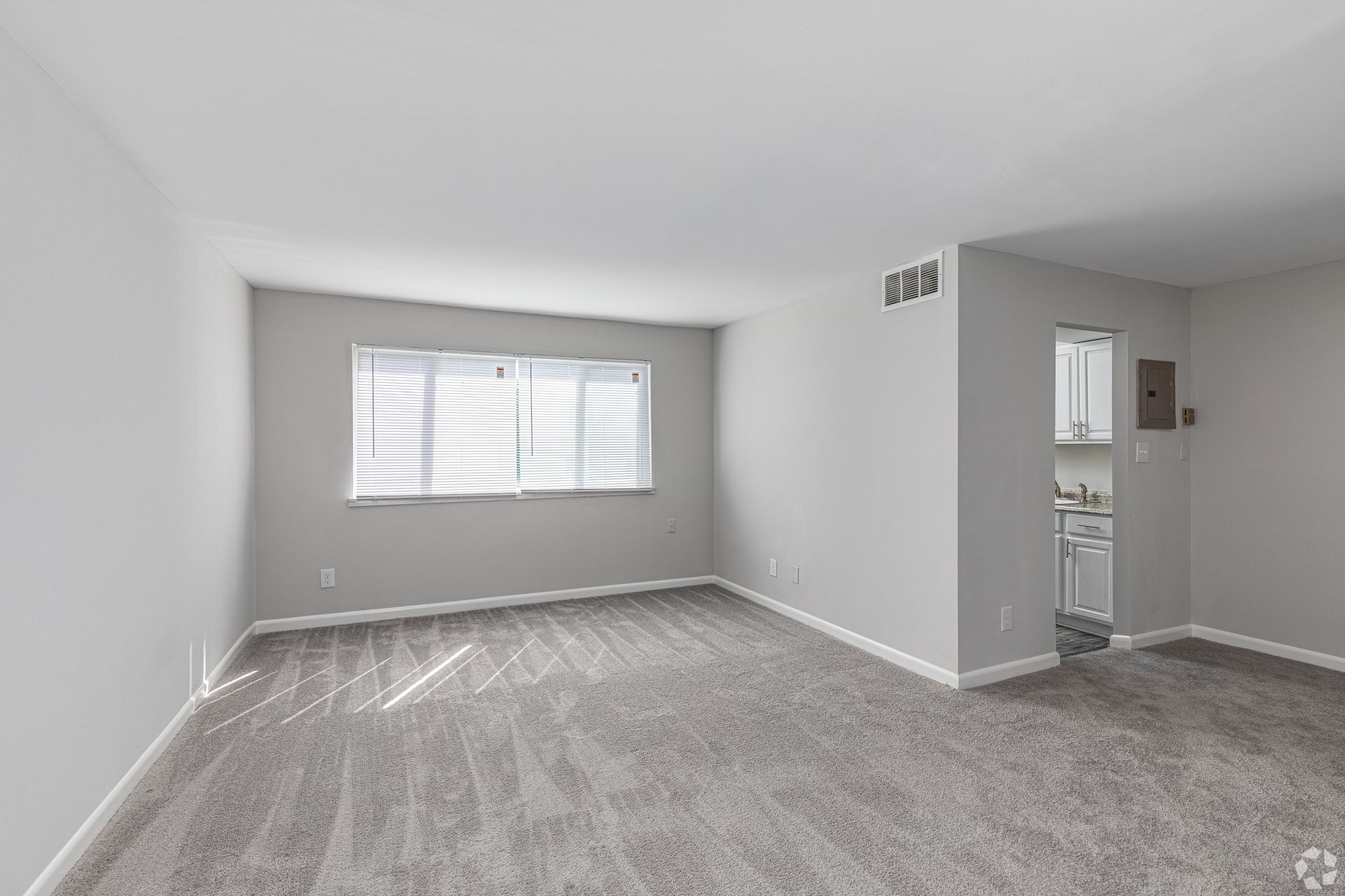 An empty living room with a carpeted floor and a window.