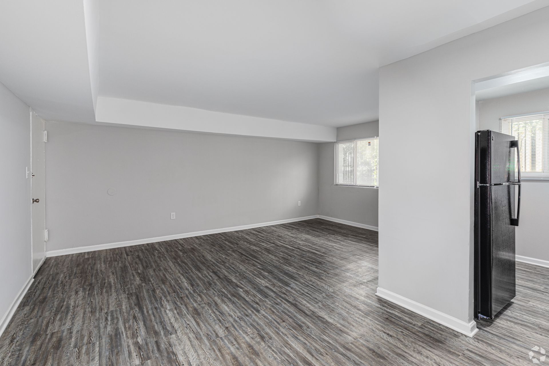 An empty living room with hardwood floors and a refrigerator.