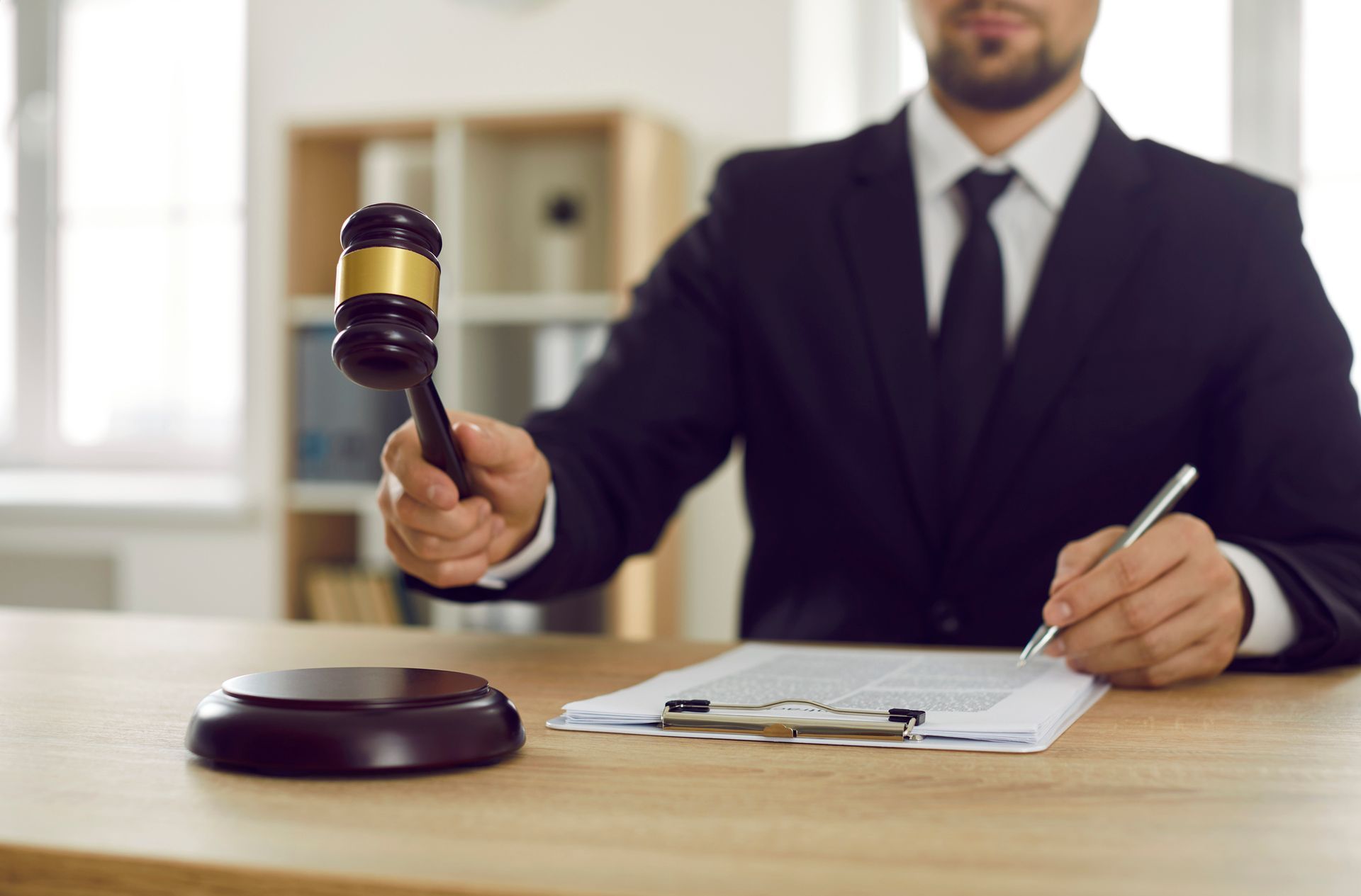 Serious male judge in his office hitting judge's gavel on sound block. Serious male judge in his office hitting judge's gavel on sound block.