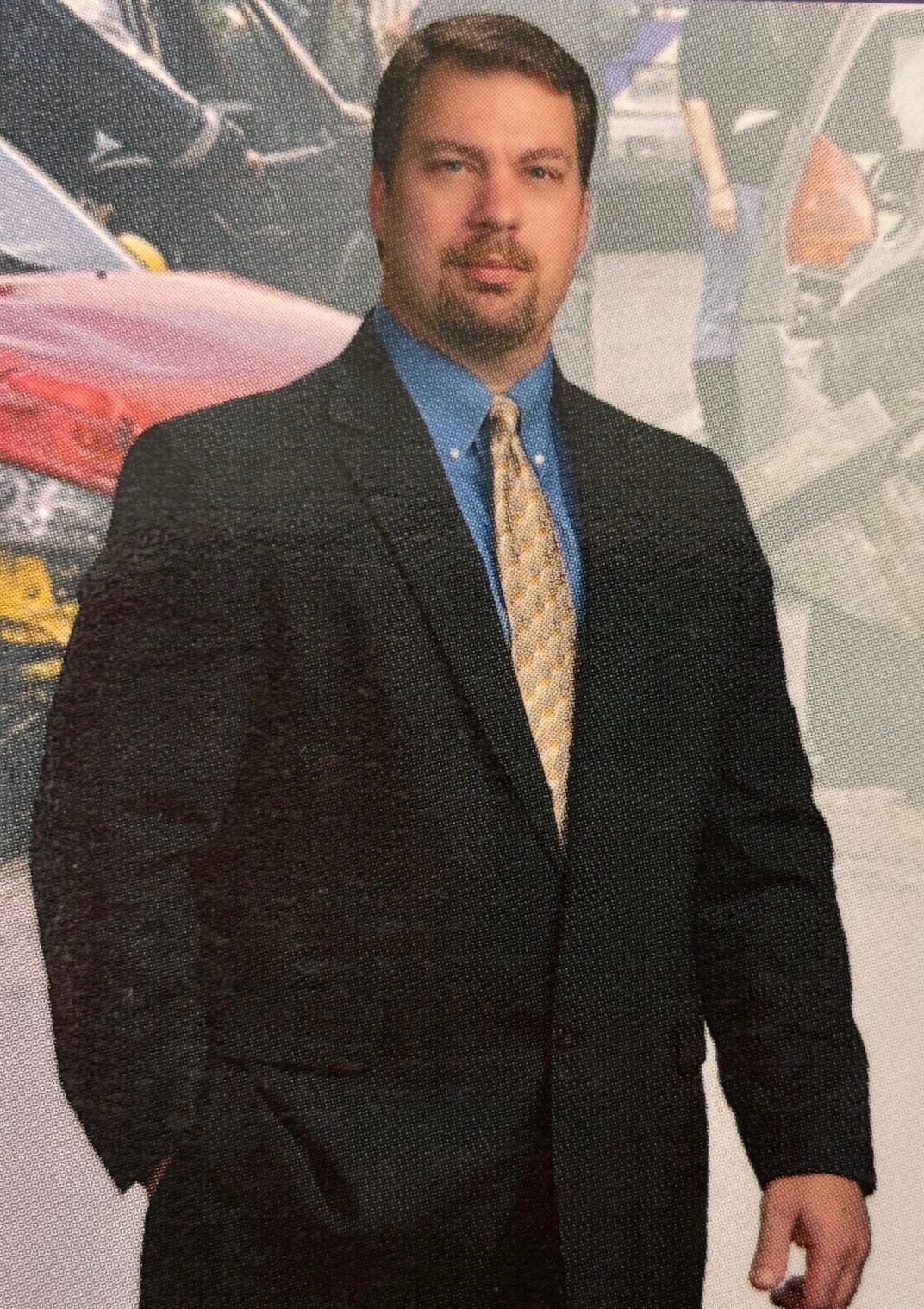 A man in a suit and tie is standing in front of a brown background. A man in a suit and tie is standing in front of a brown background.