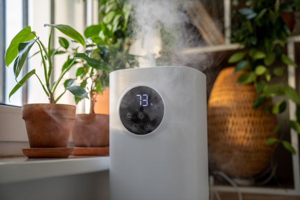 A humidifier is sitting on a window sill next to potted plants.