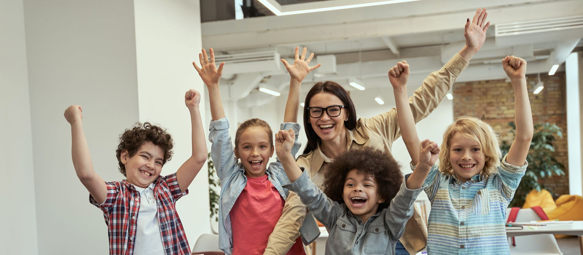 Children and teacher raising hands and smiling in a bright classroom