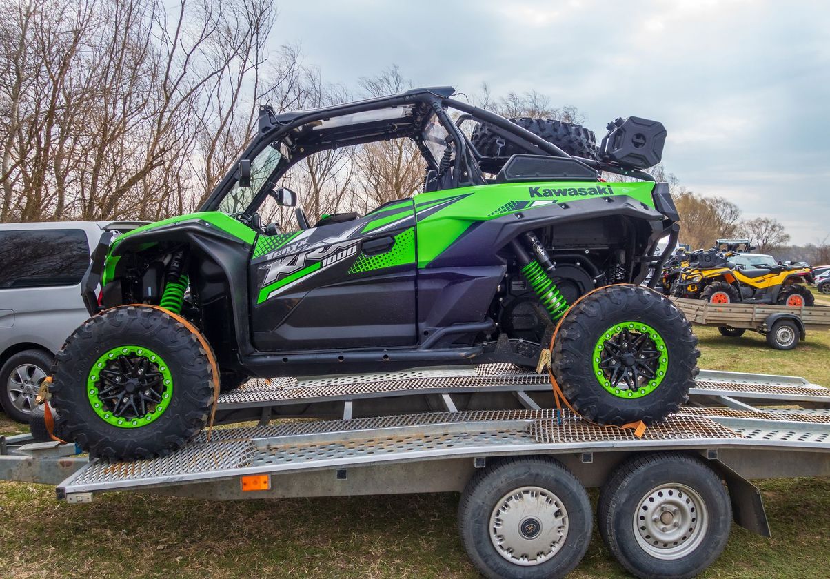 A green and black atv is sitting on top of a trailer.