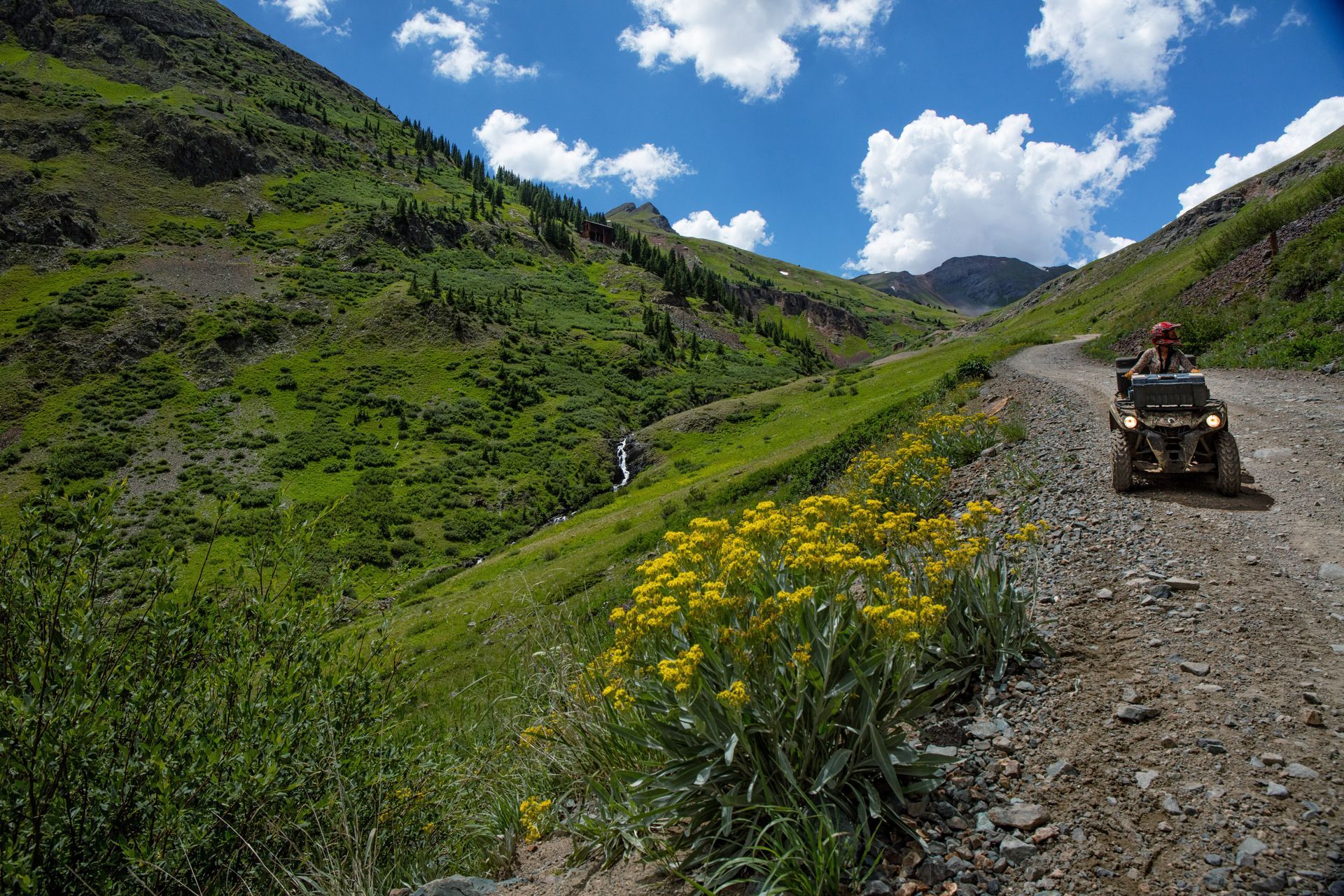 A person is riding an atv down a dirt road in the mountains.