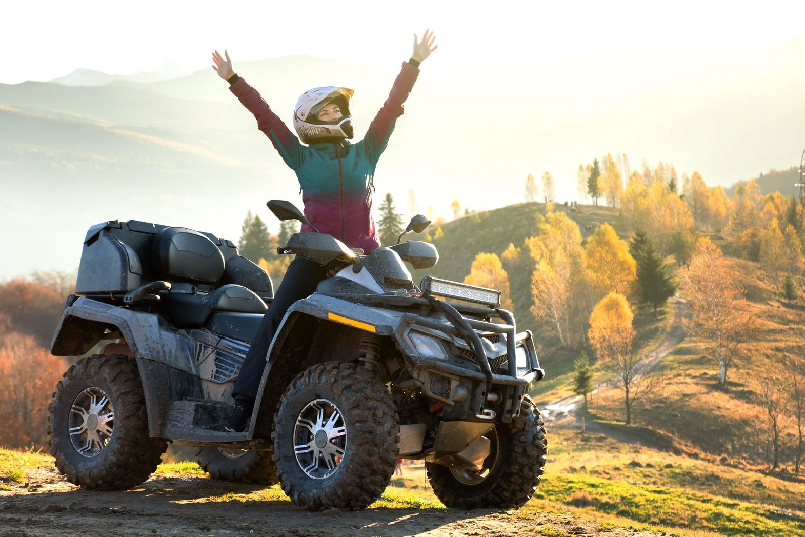A woman is riding an atv in the mountains with her arms in the air.