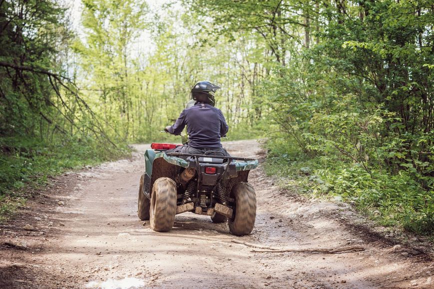 A man is riding an atv on a dirt road in the woods.